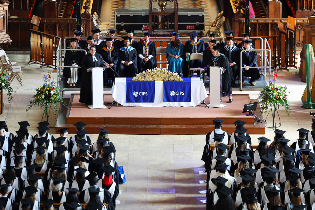A wide view of the CIPS graduation ceremony in a large hall with graduates seated and officials on a stage