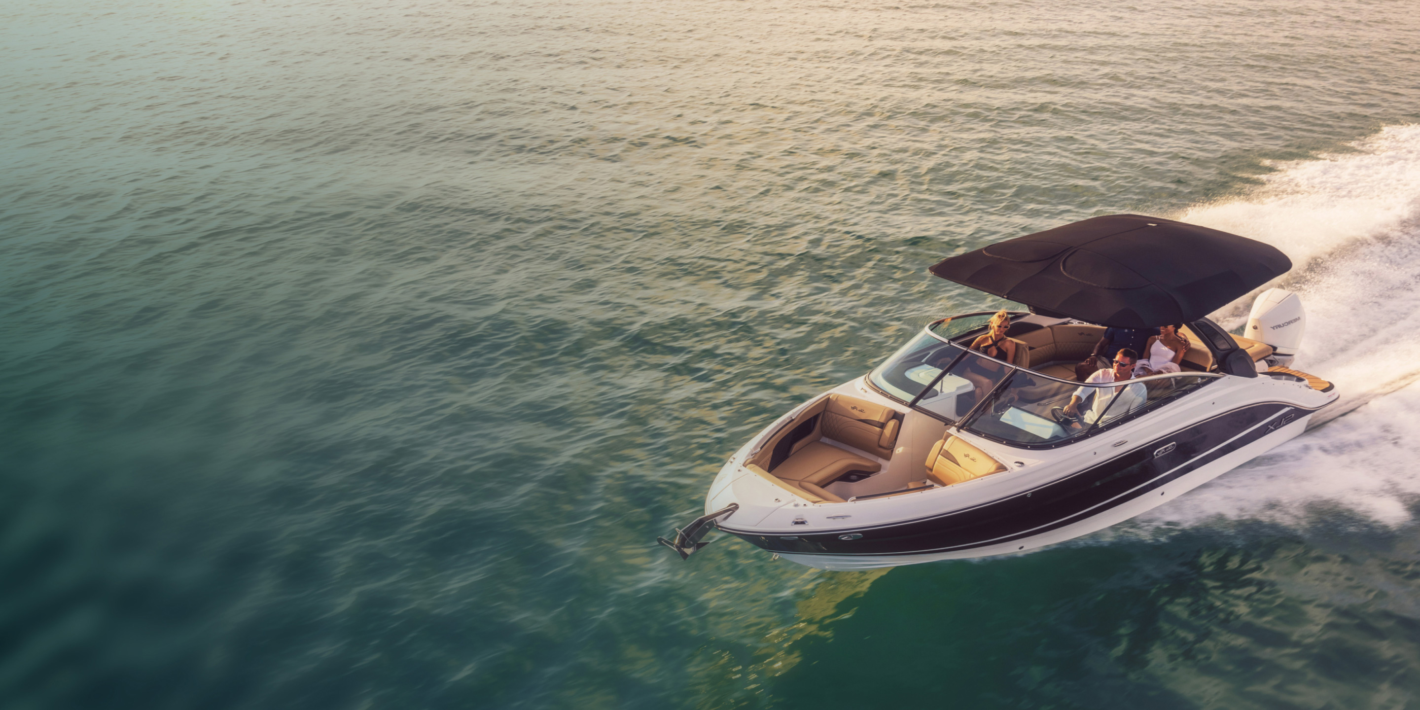 Friends speeding across water in a white and black powerboat at sunset