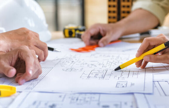 Architects looking over and making notes on blueprints laying on a table