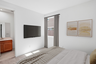 bedroom with a large bed, mounted tv, and framed yellow art pieces
