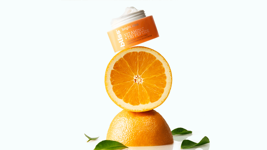Image of an orange and half of an orange stacked on top of each other with a skin cream container at the top. 
