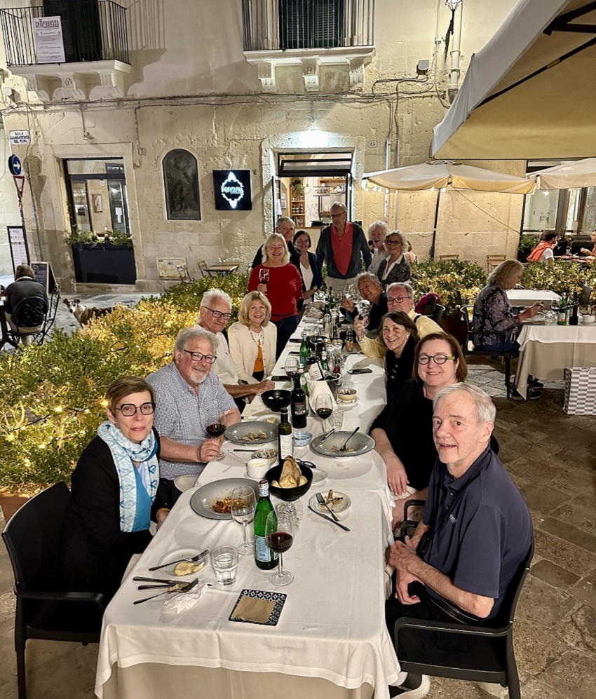The group smiles for a photo while sitting down to dinner at an outdoor restaurant