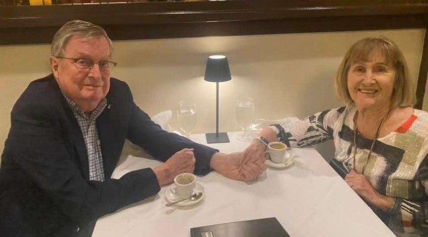 Joan and Jack holding hands at a dinner table