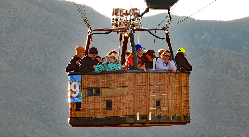 A group of people enjoy the view from a hot air balloon basket flying over the mountains in Albuquerque.
