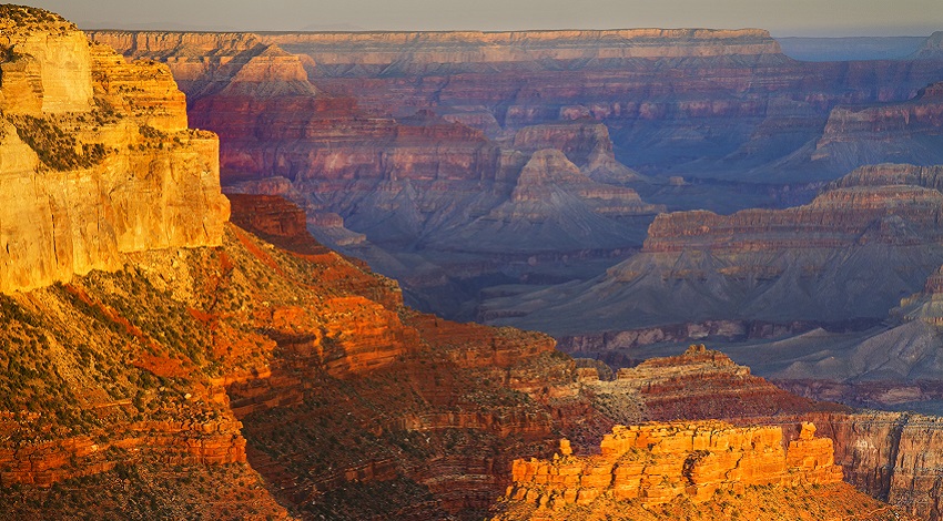 The Grand Canyon at sunrise, filled with golden yellows, reds, and blues