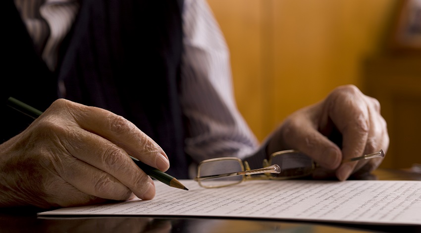 Hands holding a pair of glasses and writing on a piece of paper