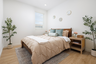 bedroom with wood floors, two potted olive plants, and tan bedding with two aqua velvet pillows