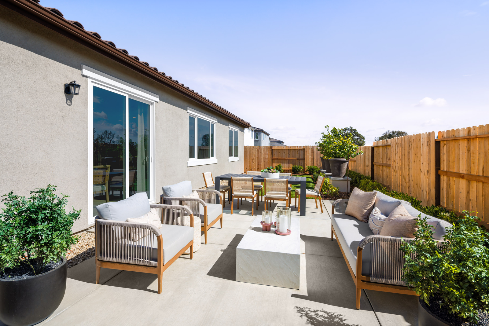 backyard with large concrete patio, gray outdoor furniture, and multiple potted plants