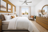 bedroom with round mirror above large wood dresser, tan upholstered bed with white bedding, and window looking out the backyard