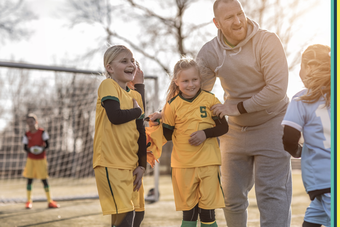 Two little girls smiling and laughing outside on a soccer field in uniform 