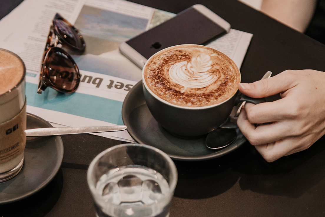 Image of coffees on a table with paper, phone, sunglasses