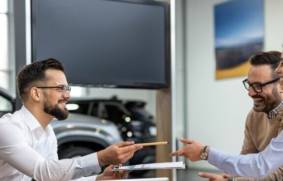 Car salesman giving a pen to a couple in a car dealership