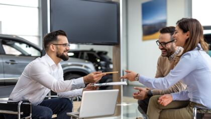 Car salesman giving a pen to a couple in a car dealership