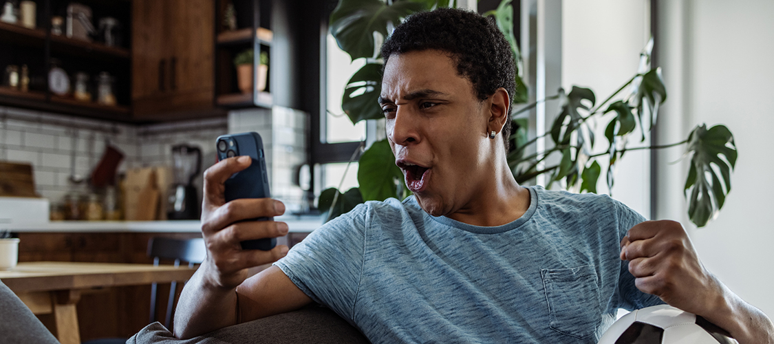 A young Black man cheers while looking at his phone