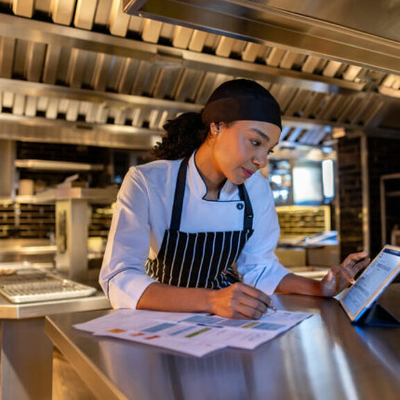 Chef in a kitchen reviewing paperwork and a tablet