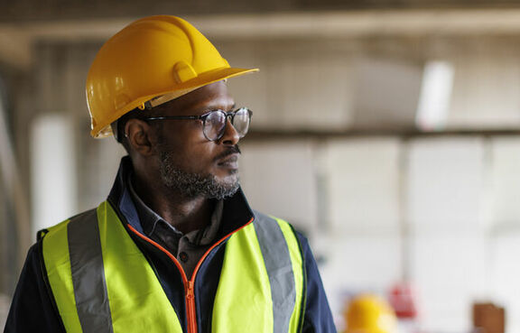 Male construction worker in a yellow safety vest and hard hat using a tablet at a worksite