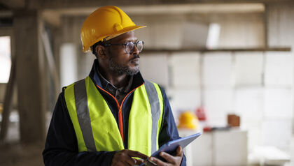 Male construction worker in a yellow safety vest and hard hat using a tablet at a worksite
