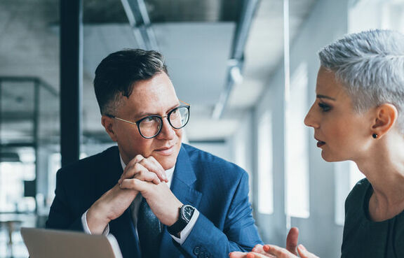 Co-workers sitting at a table talking and looking at a laptop