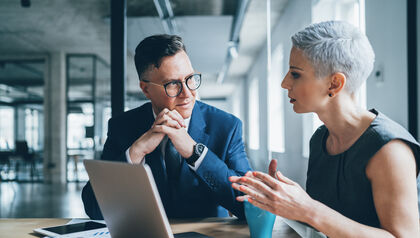 Co-workers sitting at a table talking and looking at a laptop