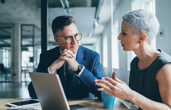 Co-workers sitting at a table talking and looking at a laptop
