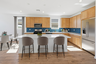 spacious kitchen with light brown cabinets, quartz countertops, and grey barstools