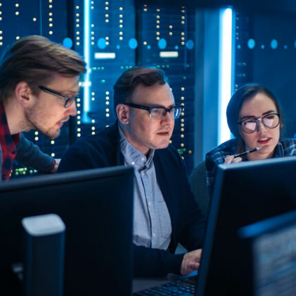 Three people looking at a computer in a server room