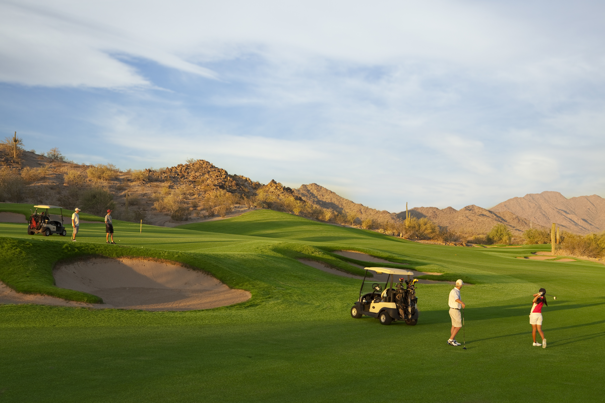 golf course with golfers, surrounded by mountains 