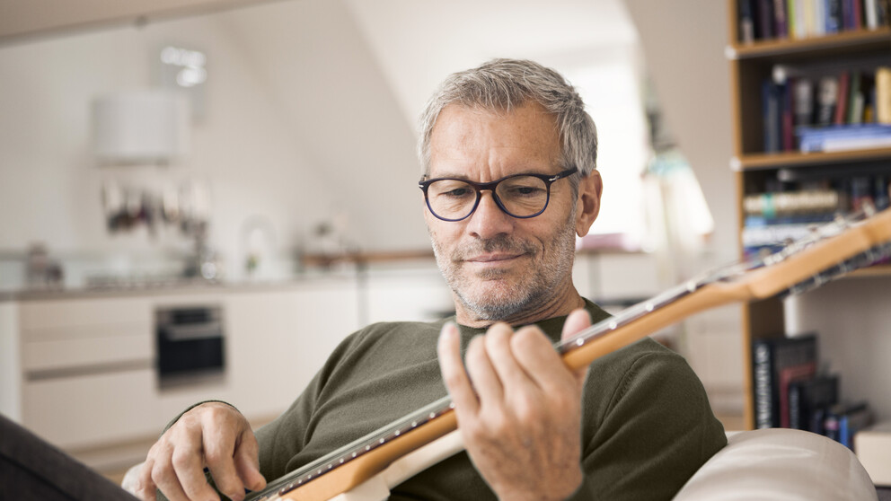 Oude man draagt ​​HOYA-progressieve lenzen terwijl hij gitaar speelt