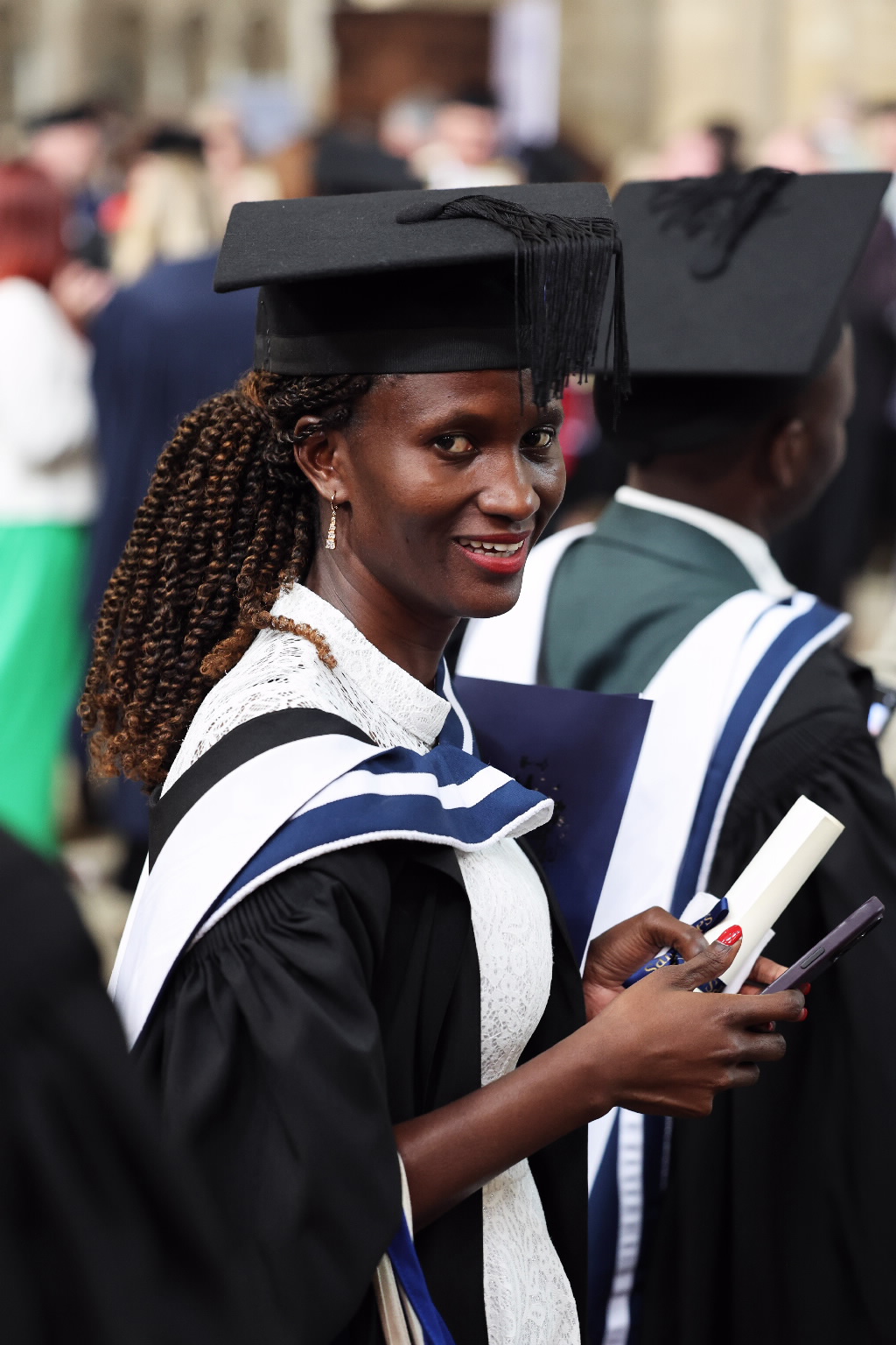 Female graduate in cap and gown, with braided hair, smiling