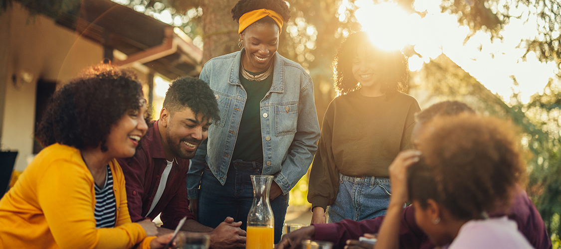 A Black family laughs together around a table outside
