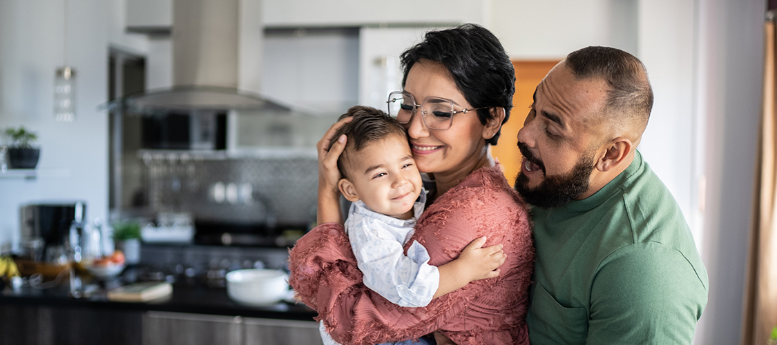 A Hispanic woman and man play with a smiling baby in their kitchen
