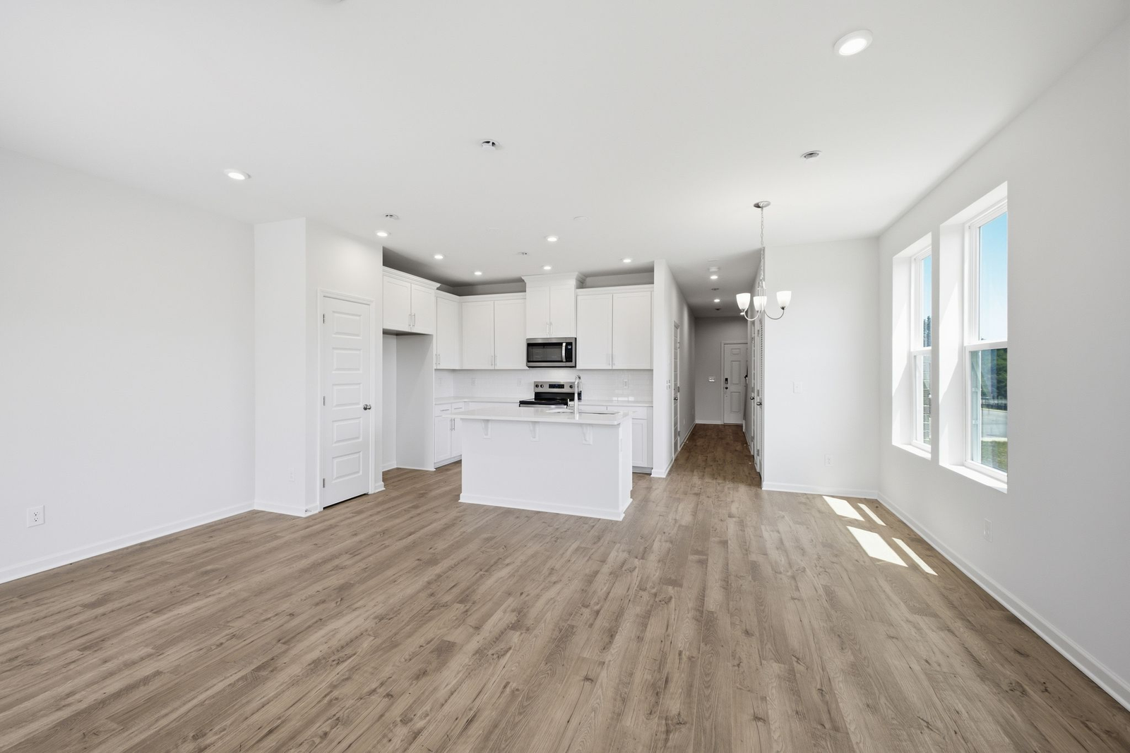great room with hardwood floors and large windows attached to open concept kitchen with white cabinets and stainless steel appliances