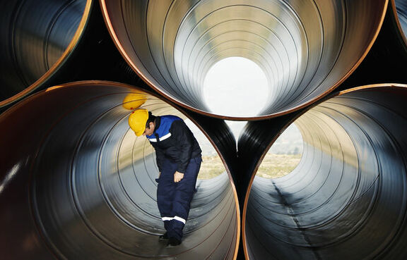 Large metal tubes stacked with a man inspecting one