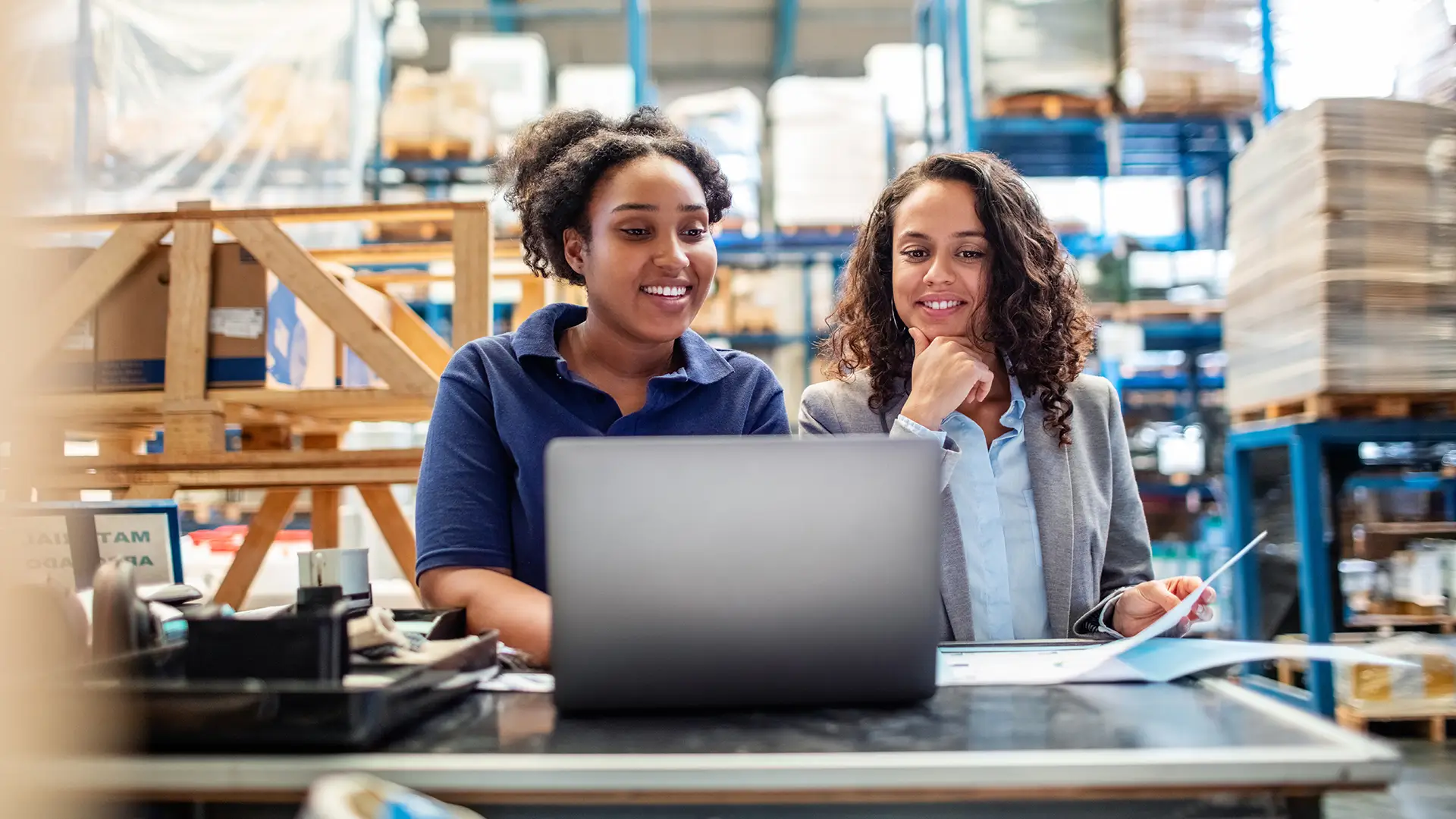 Two females in a warehouse smiling and looking at a computer
