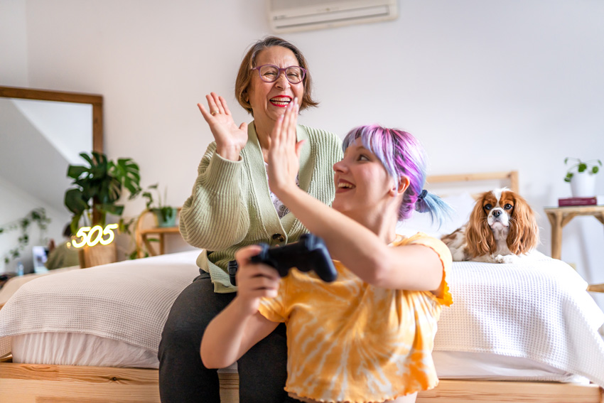 Prikupen medgeneracijski trenutek med babico in vnukinjo, ki igrata računalniške igrice.