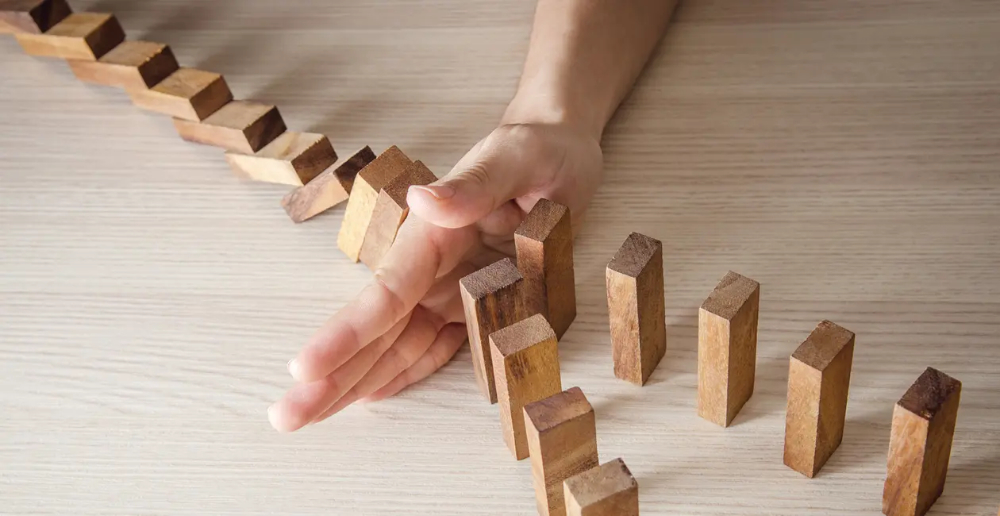 Blocks stood up like dominoes going from one row and splitting into two rows with a hand stopping at the split so they can't fall over into them 