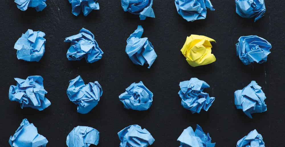 Shows rows of scrunched up paper set equally apart, all are blue apart from one; which is yellow. 