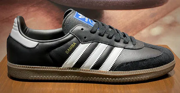 A photo of an Adidas Samba black and white trainer/sneaker, side on view, on a wooden surface