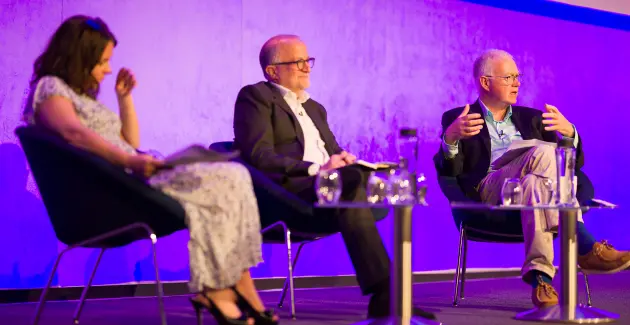 Panel discussion with three speakers seated on stage at a procurement and supply chain conference.