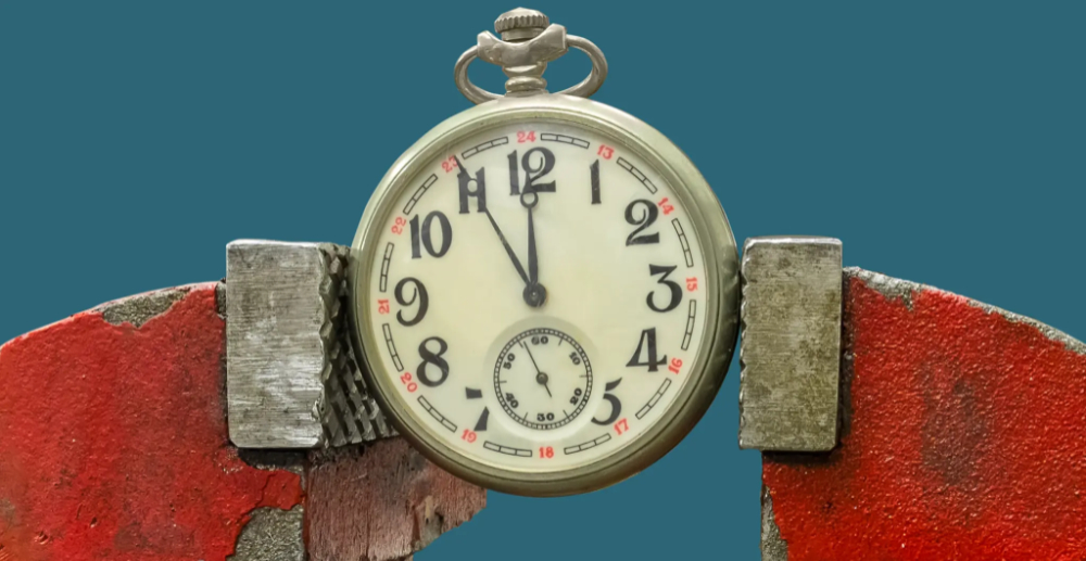 An old looking pocket watch held in a clamp, the watch shows the time as 11:55. 