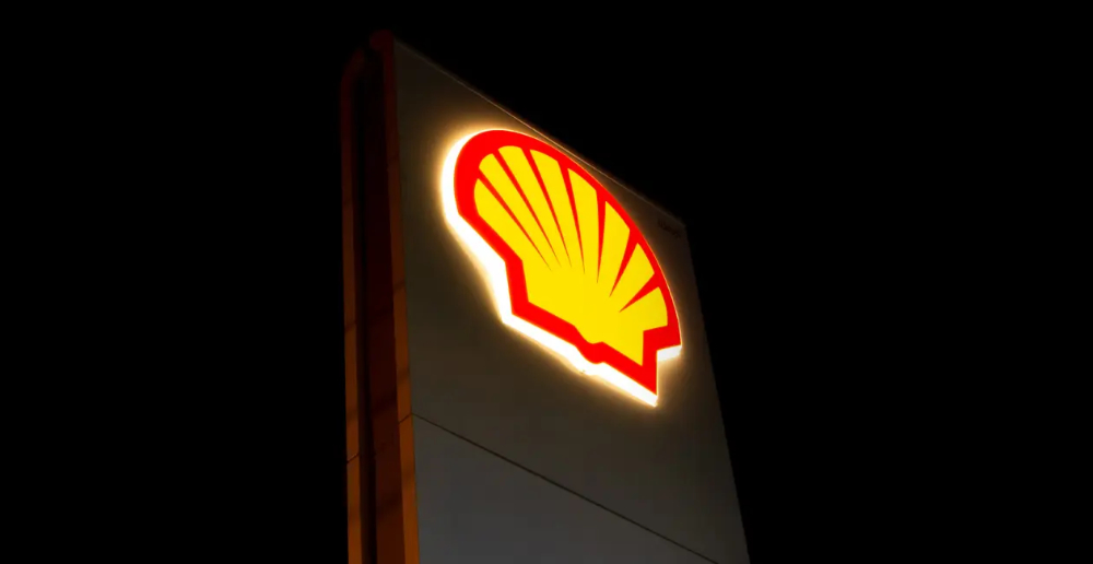 A nighttime photo of the lit up shell logo on a structure