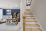 entryway with light wood floors, study with blue accent wall, and wood stairs with oak railing