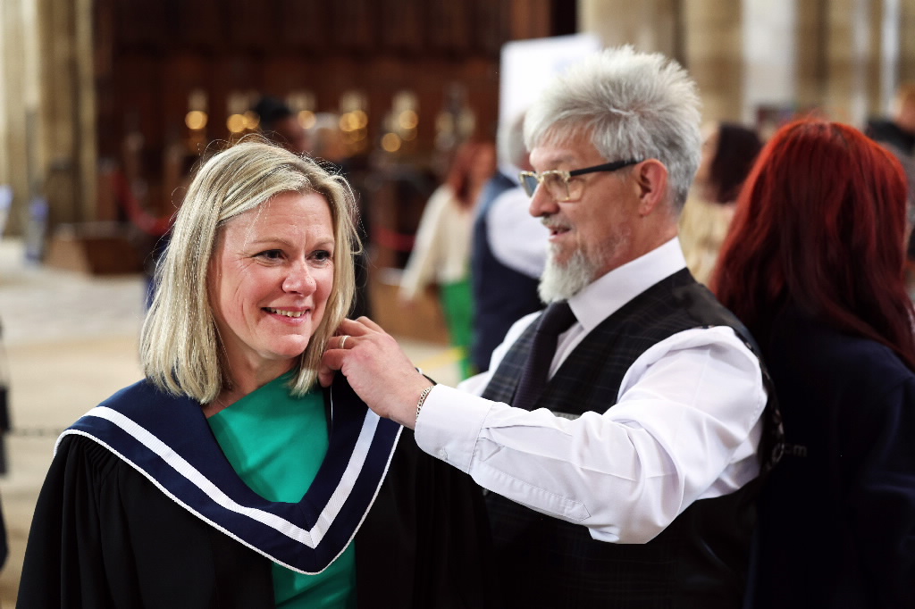 Man adjusting the academic hood of a smiling female graduate.