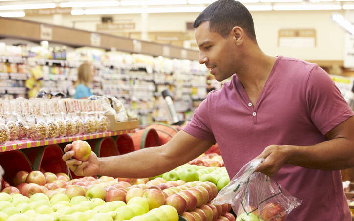 A man selecting apples in a grocery store produce section.