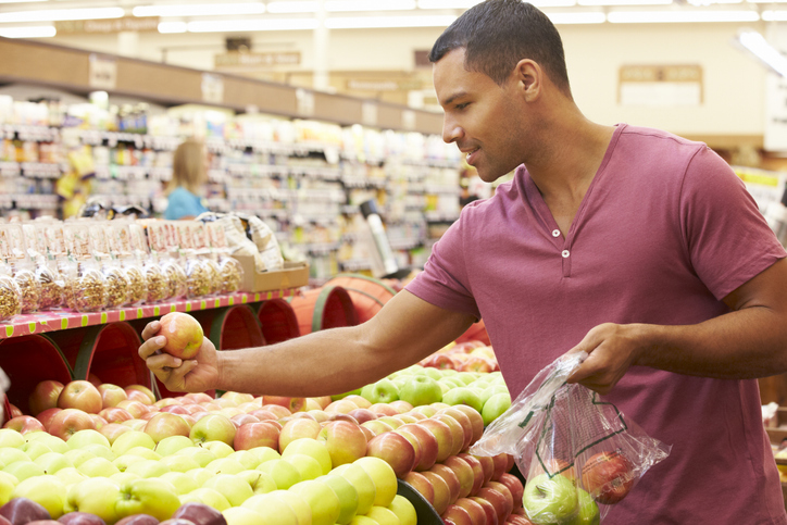 A man selecting apples in a grocery store produce section.