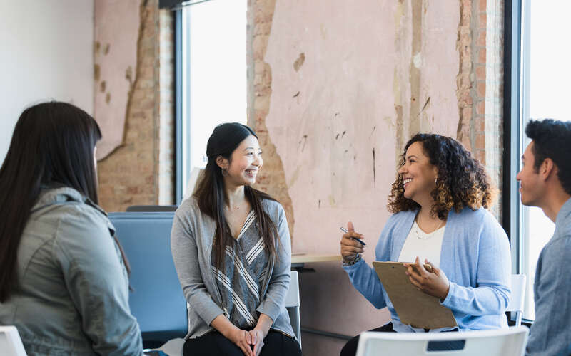 The adult female manager smiles and gestures as she leads a meeting for her diverse staff.