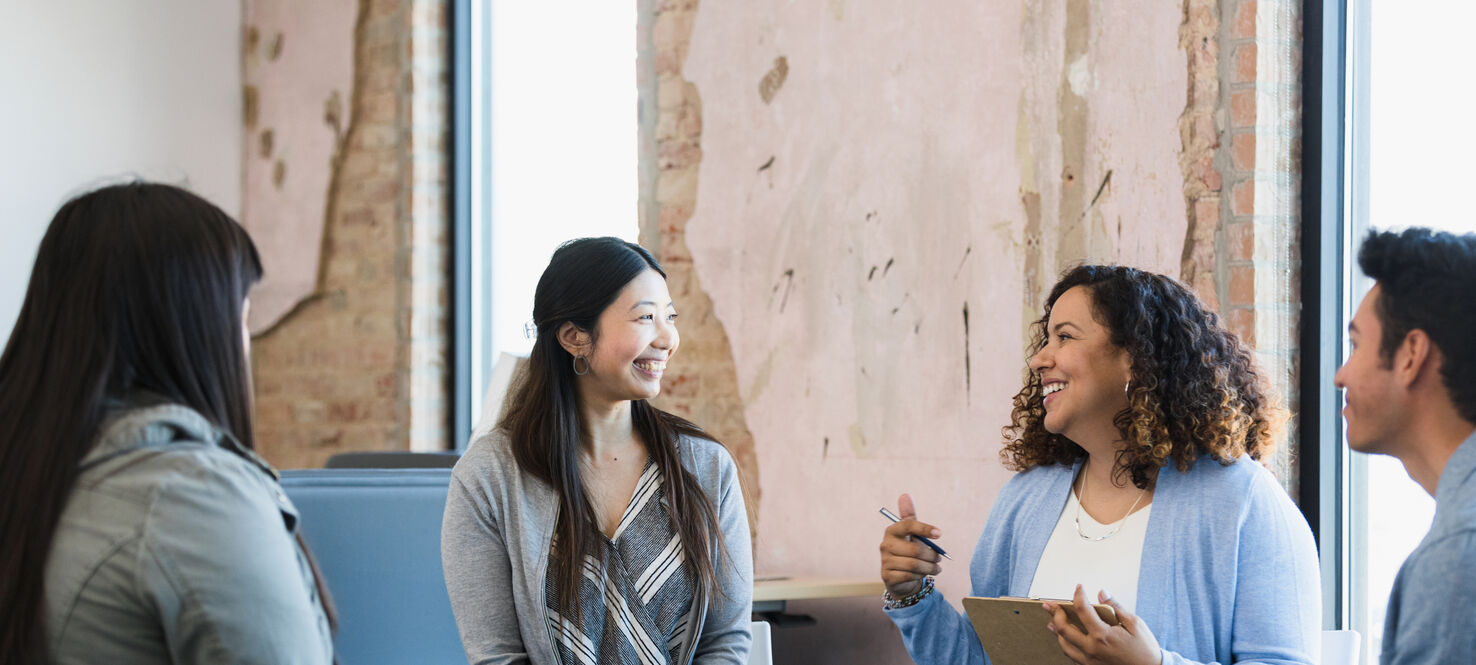The adult female manager smiles and gestures as she leads a meeting for her diverse staff.