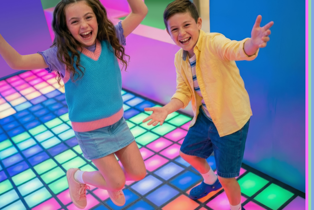 Two children jumping and playing on light up neon play zone floor.