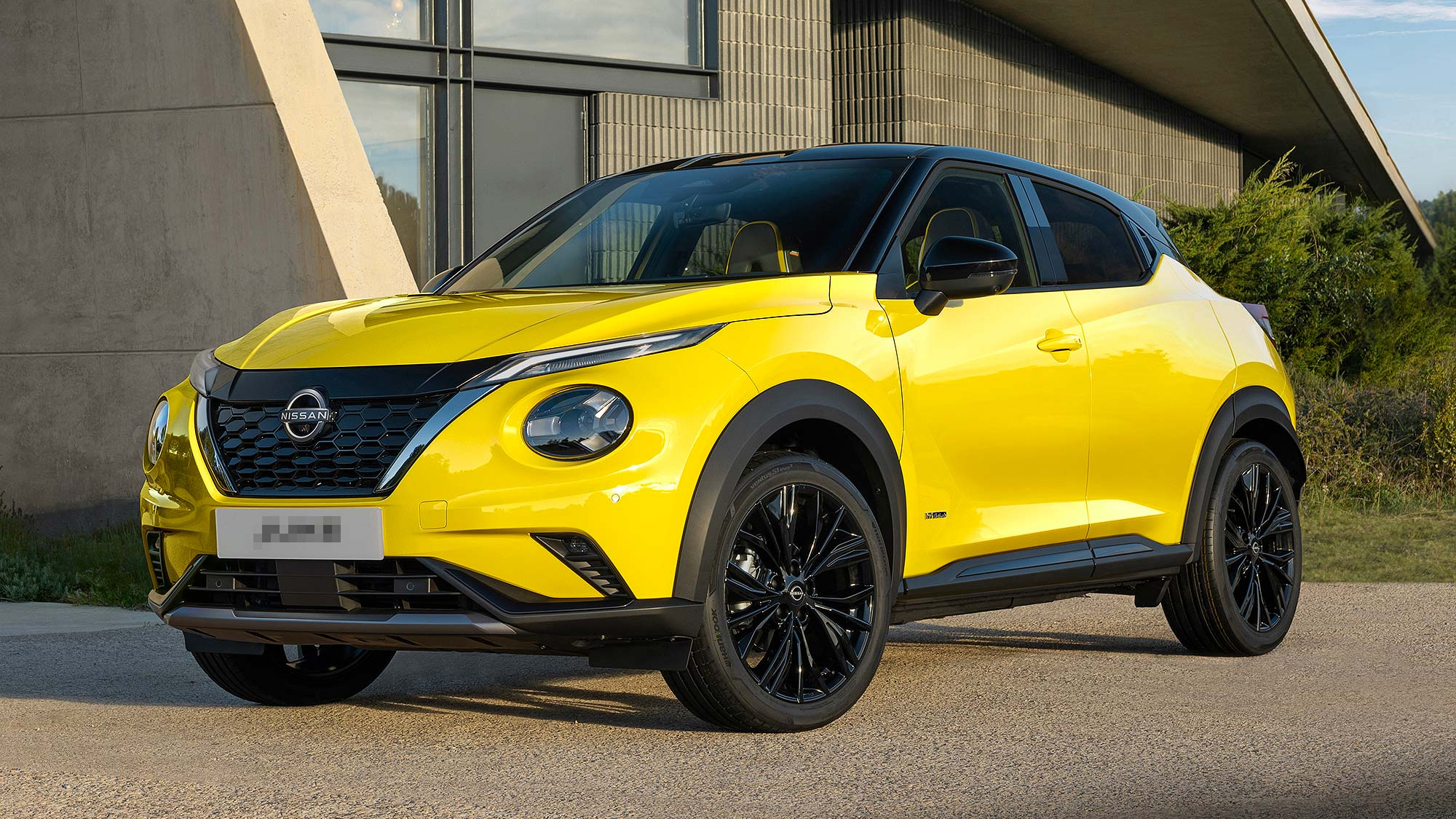 Yellow Nissan Juke compact SUV parked outside a modern building, featuring black alloy wheels and contrasting black roof.