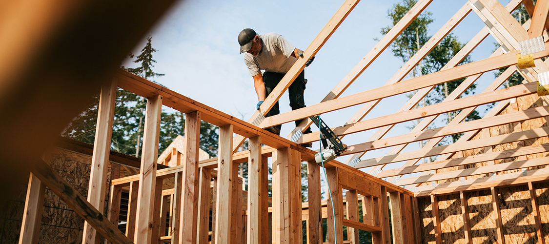 A man works on the roof of the frame of a new house